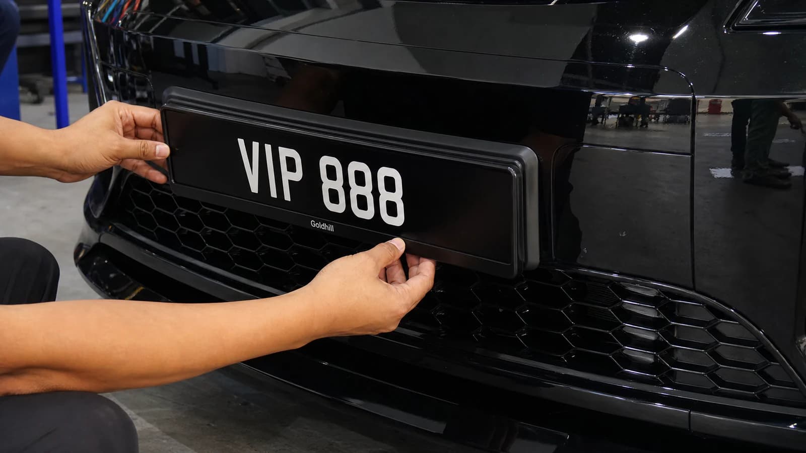 A specialist carefully fitting a long black plate into a vehicle holder